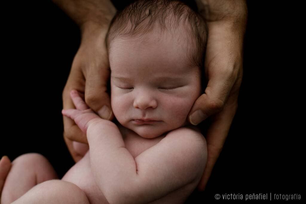newborn durmiendo sobre negro abrazado por las manos de su padre